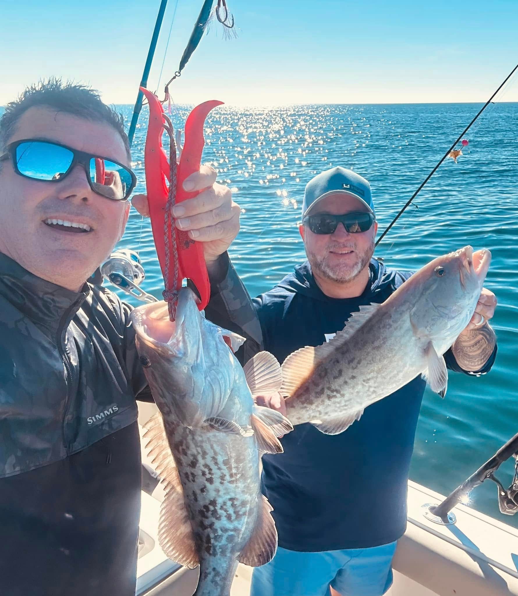 Two anglers on a boat holding two large fish on a sunny ocean trip