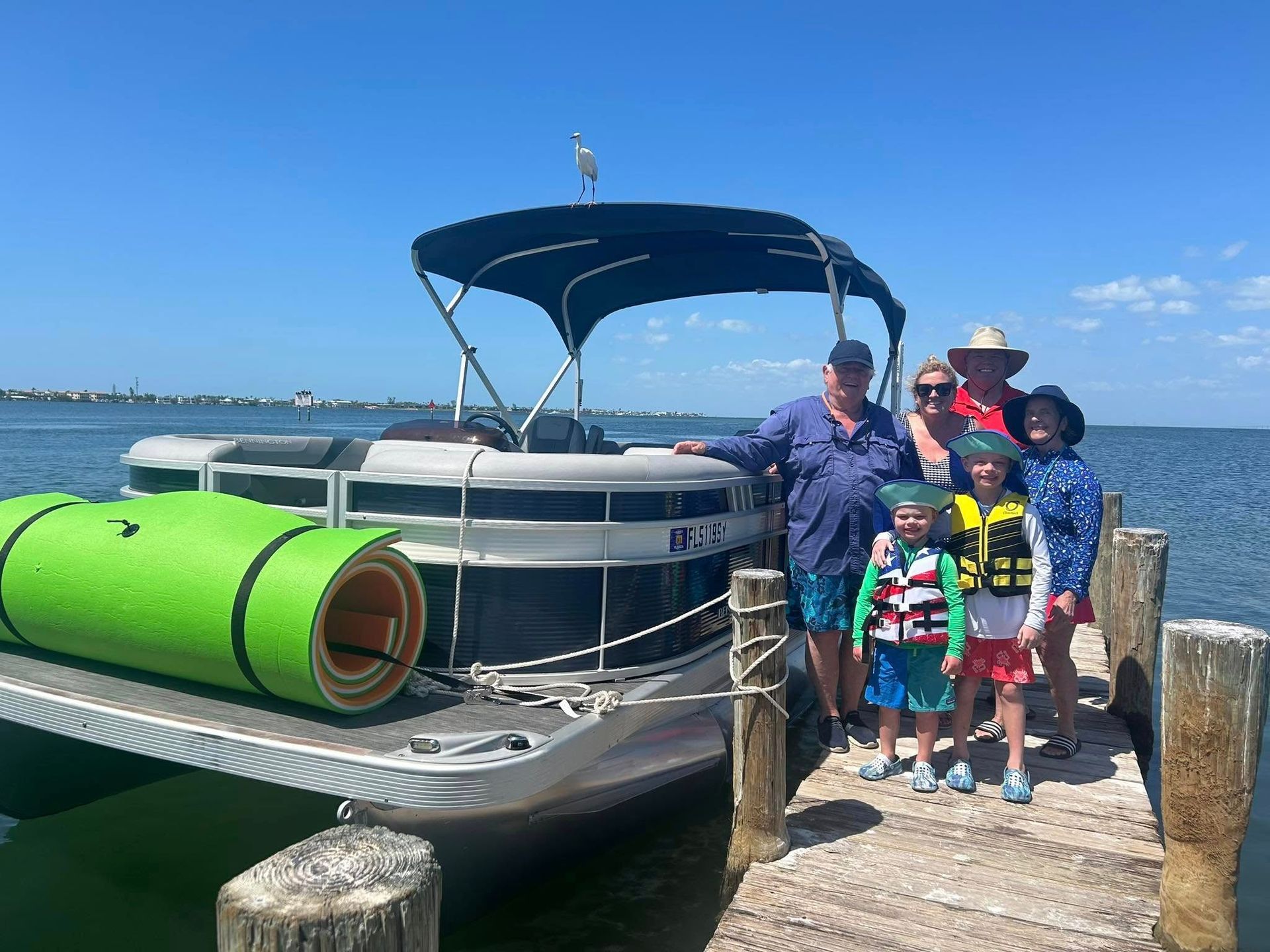 Family posing beside a pontoon boat at a marina, with a bright green kayak in the foreground.