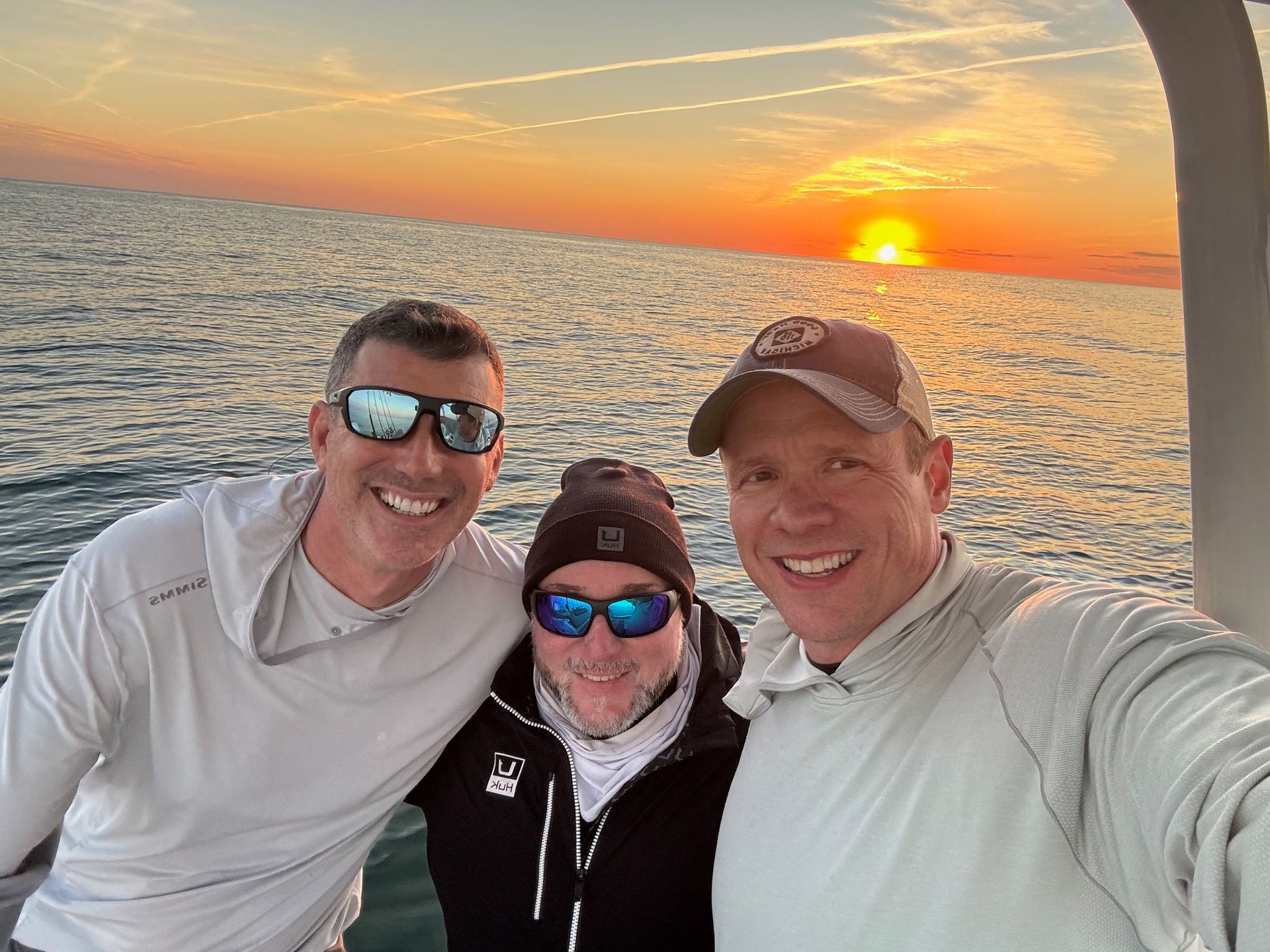Three smiling friends taking a sunset selfie on a boat at sea.