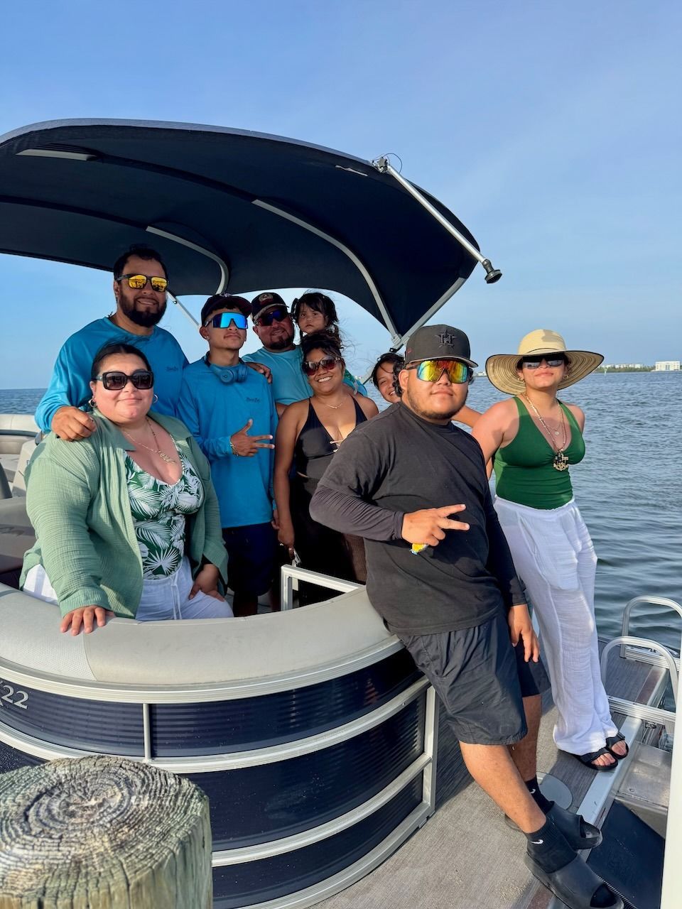 Group of people posing on a boat deck with a dark canopy, smiling near the water.