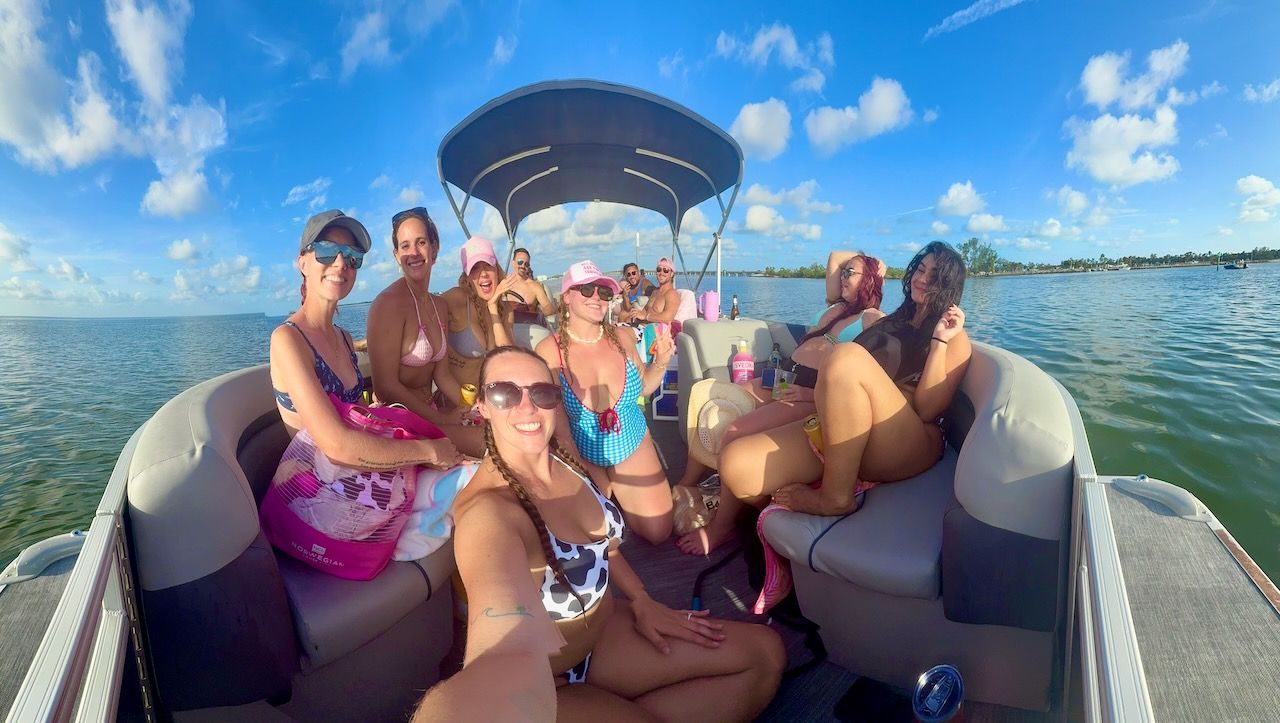 Friends smiling on a pontoon boat, relaxing on a sunny lake under a blue sky.