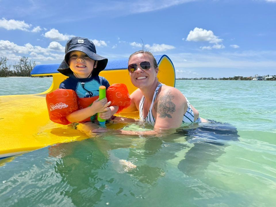 Two people smiling on a yellow kayak in clear blue water under a sunny sky.