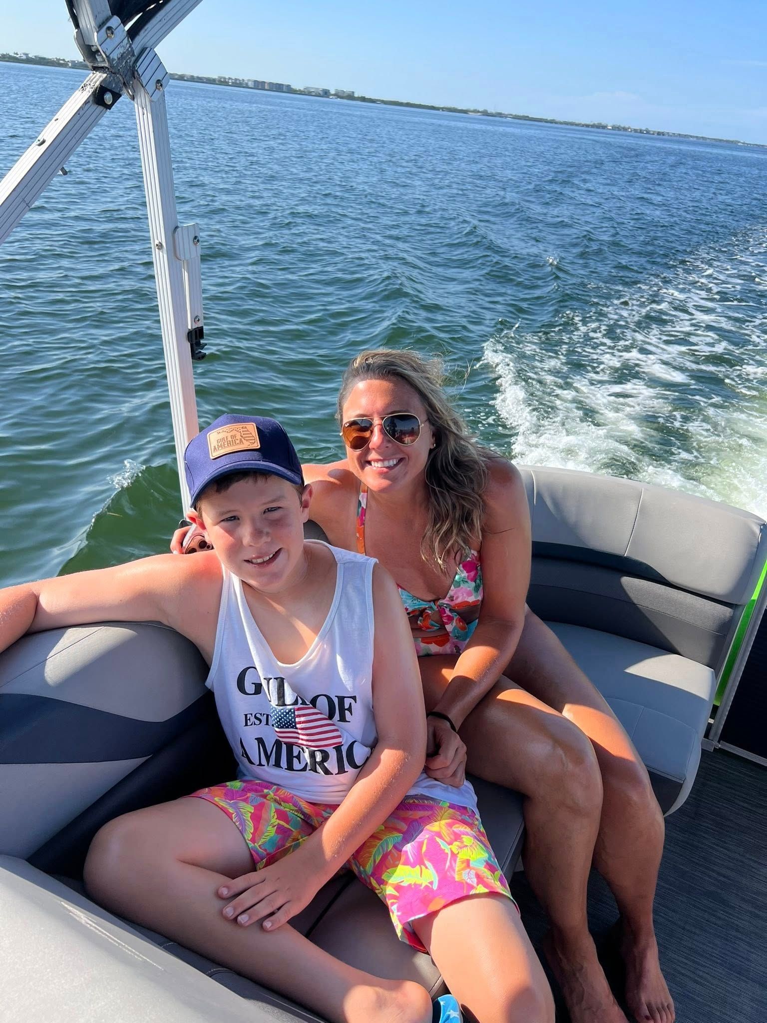 Two people smiling on a boat, with blue water and a wake behind them.