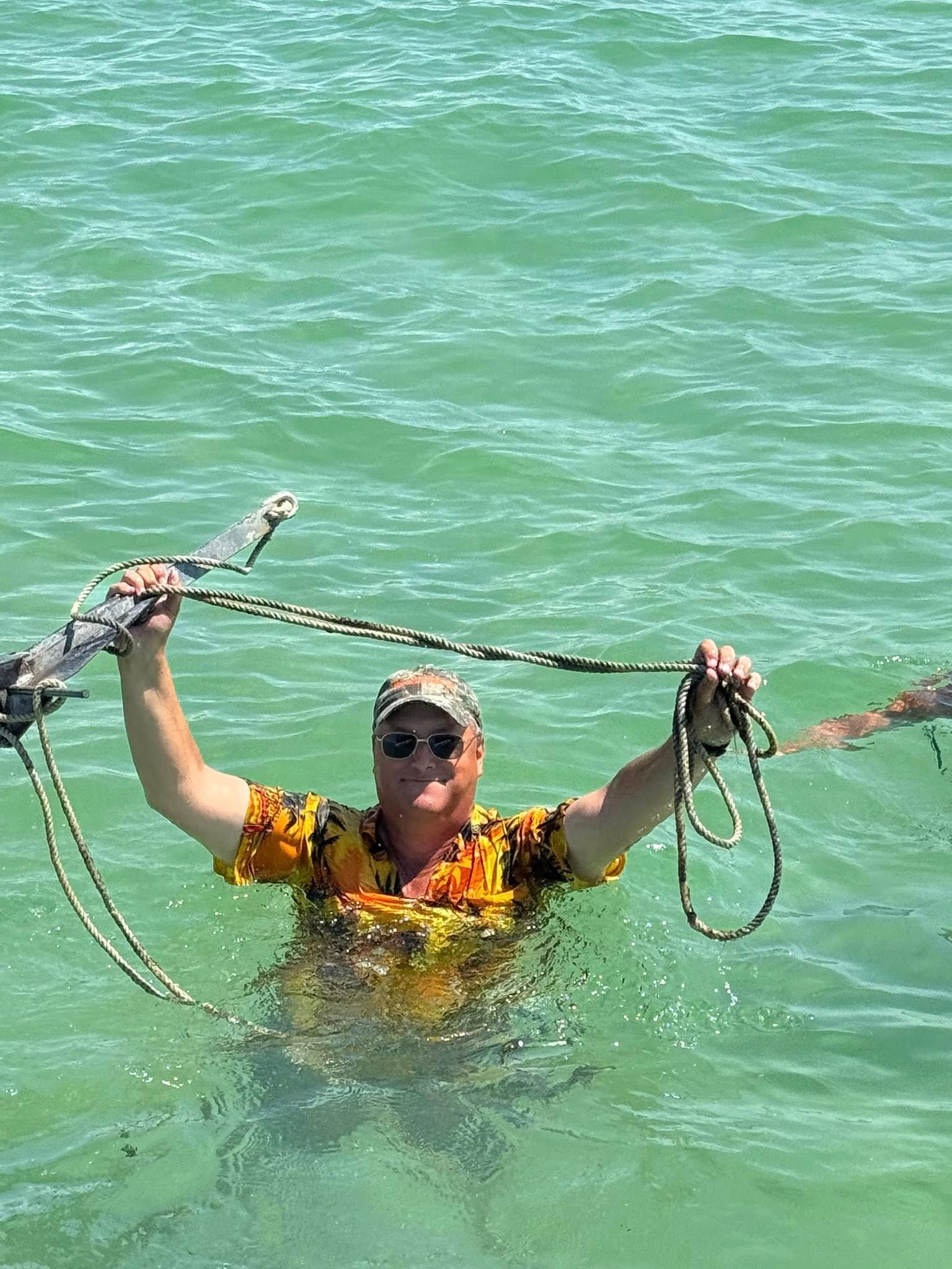 Person in orange life jacket treads water in a lake, holding boat ropes overhead.