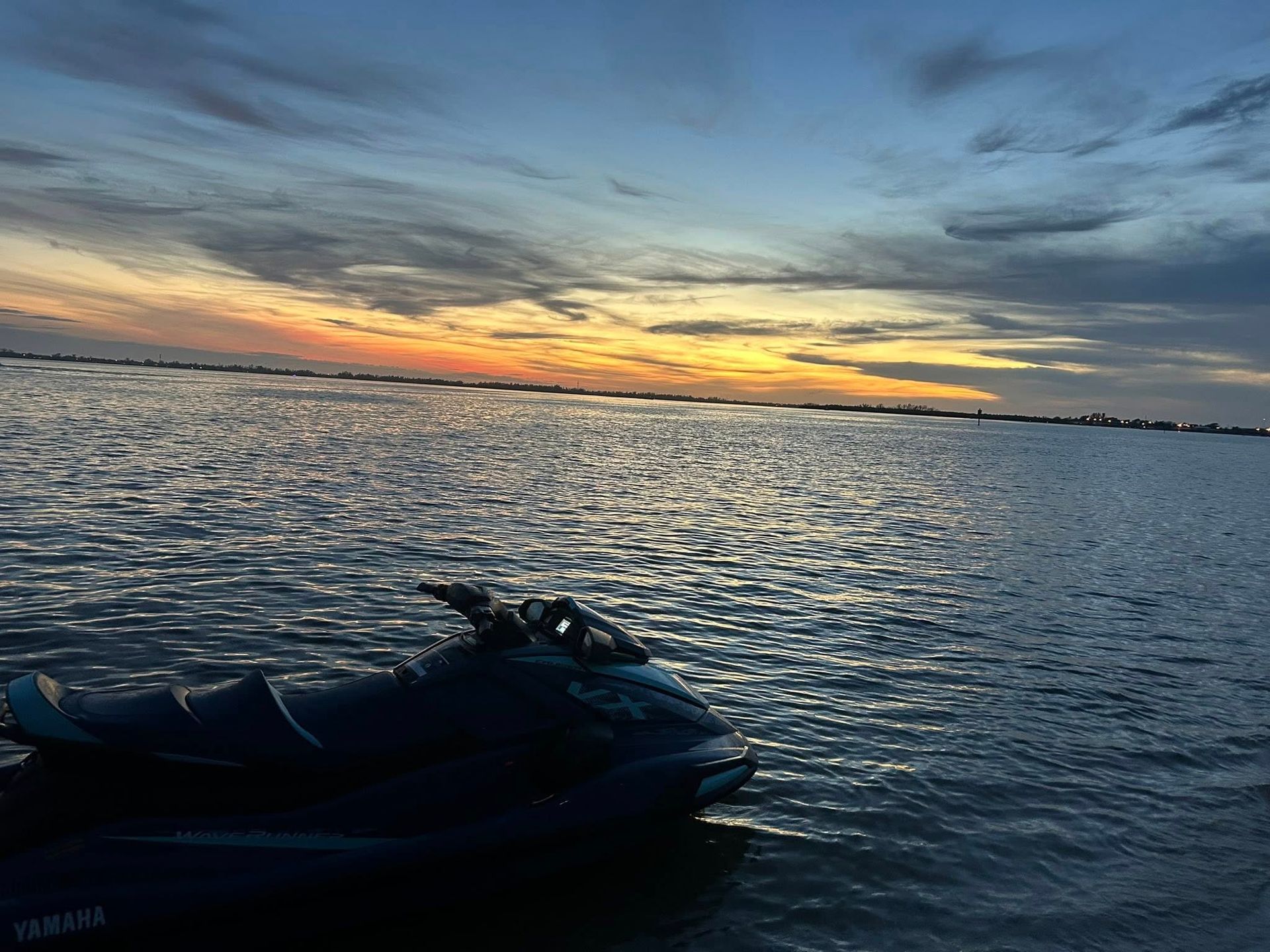 Jet ski on calm water at sunset with orange clouds and a distant shoreline