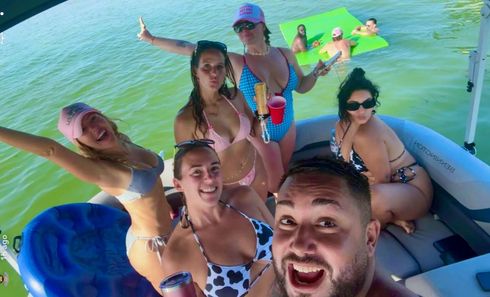 Group posing on a boat in sunny water, with a blue canopy and another boat in the background