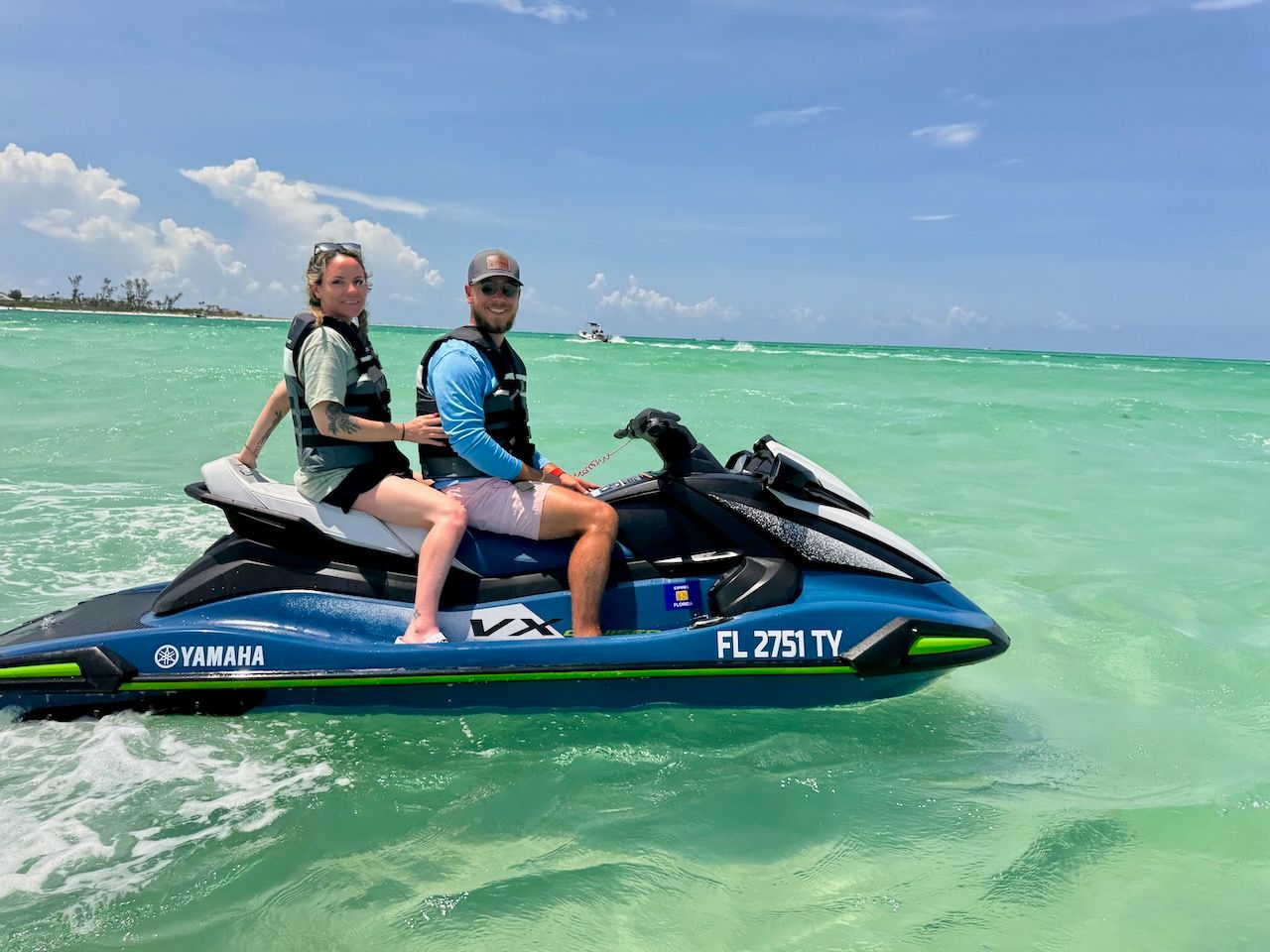 Two people riding a jet ski on clear turquoise water under a blue sky