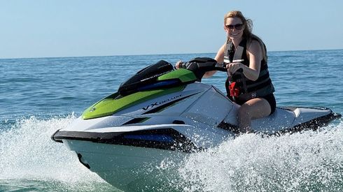 Jet skis lined up on a sunny beach beside calm water at sunset