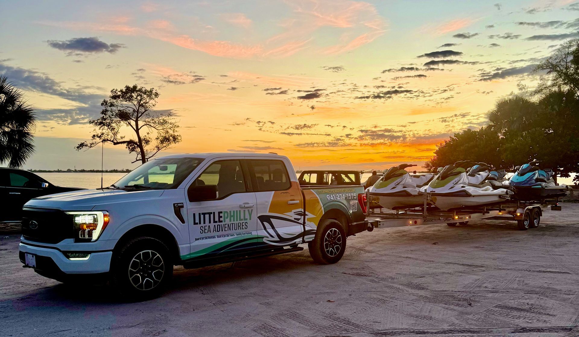 White utility pickup truck at sunset near a trailer lot, with other vehicles and debris in the background.