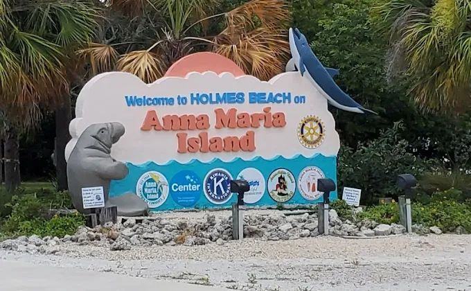 Welcome to Holmes Beach, Anna Maria Island sign in a tropical roadside setting
