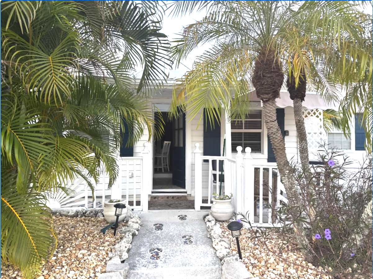 Front porch of a white house with palm trees, a stone path, and potted plants.