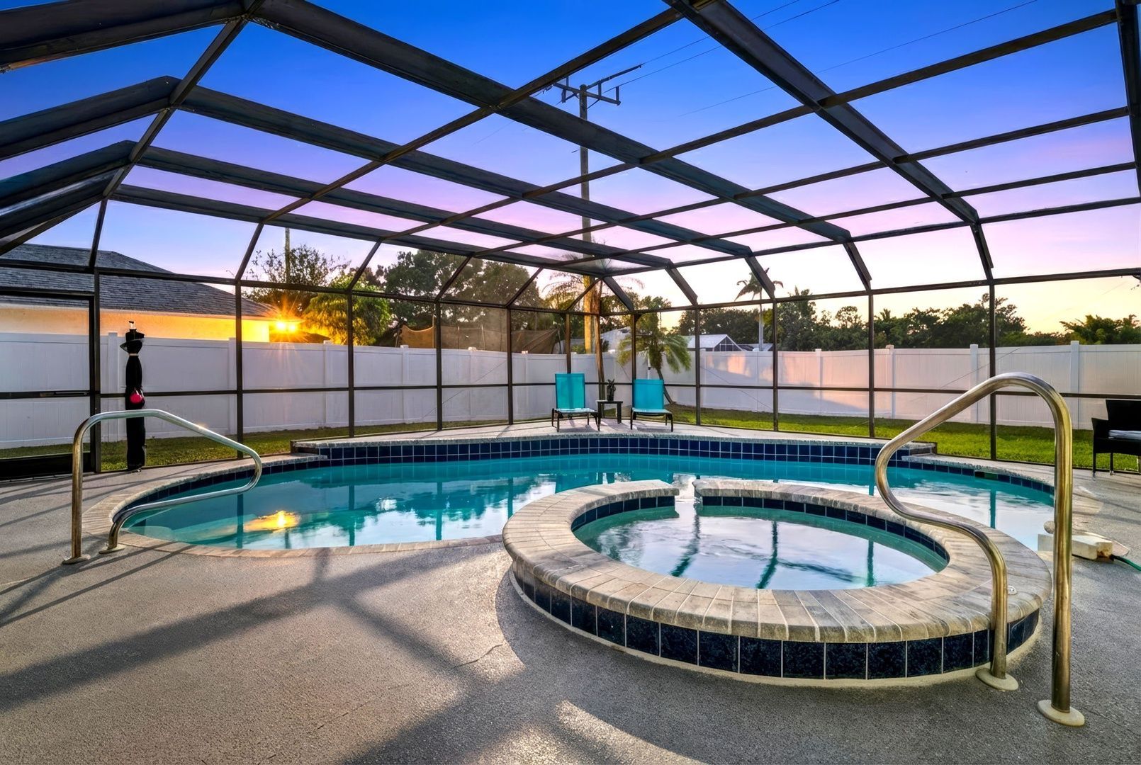 Screened-in backyard pool and hot tub at sunset with blue water and lounge chairs