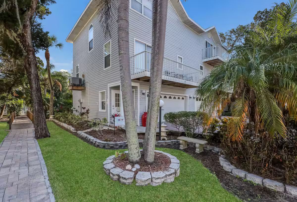 Coastal house with white siding, palm trees, and a landscaped front yard beside a walkway