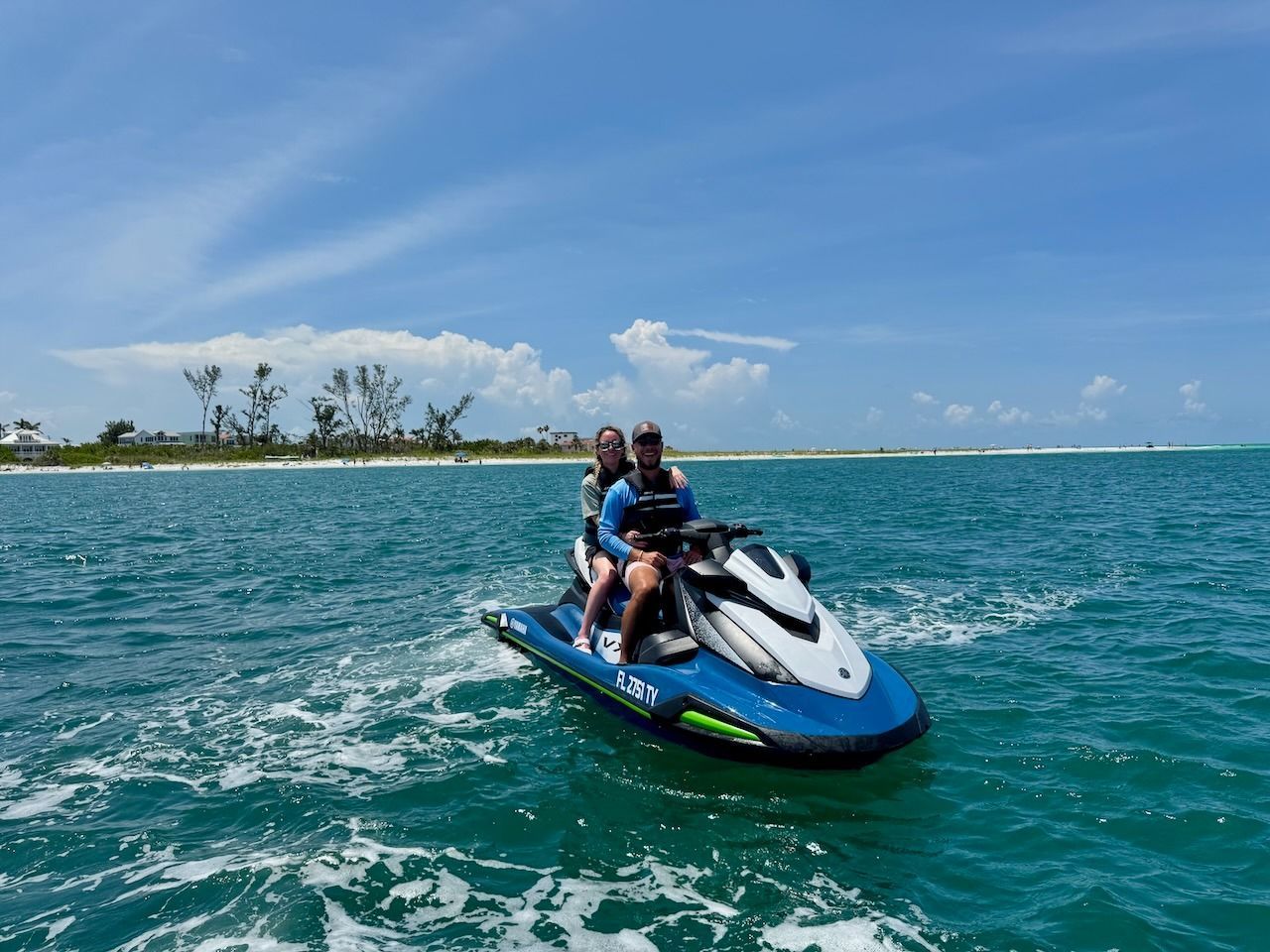 Two people riding a blue-and-white jet ski on turquoise water near a tropical shoreline