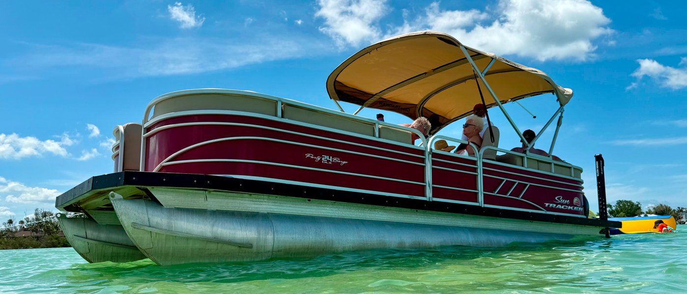 Pontoon boat with red sides and yellow canopy floating on clear blue water under a sunny sky