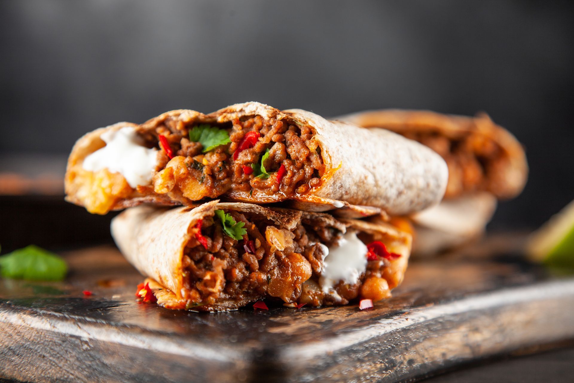 Two burritos are stacked on top of each other on a wooden cutting board.