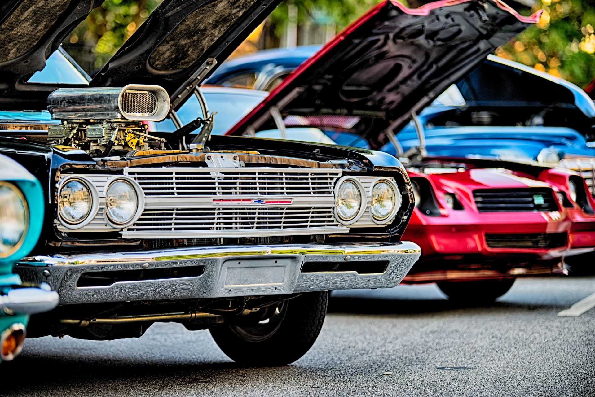 A row of cars with their hoods open are parked on the side of the road.