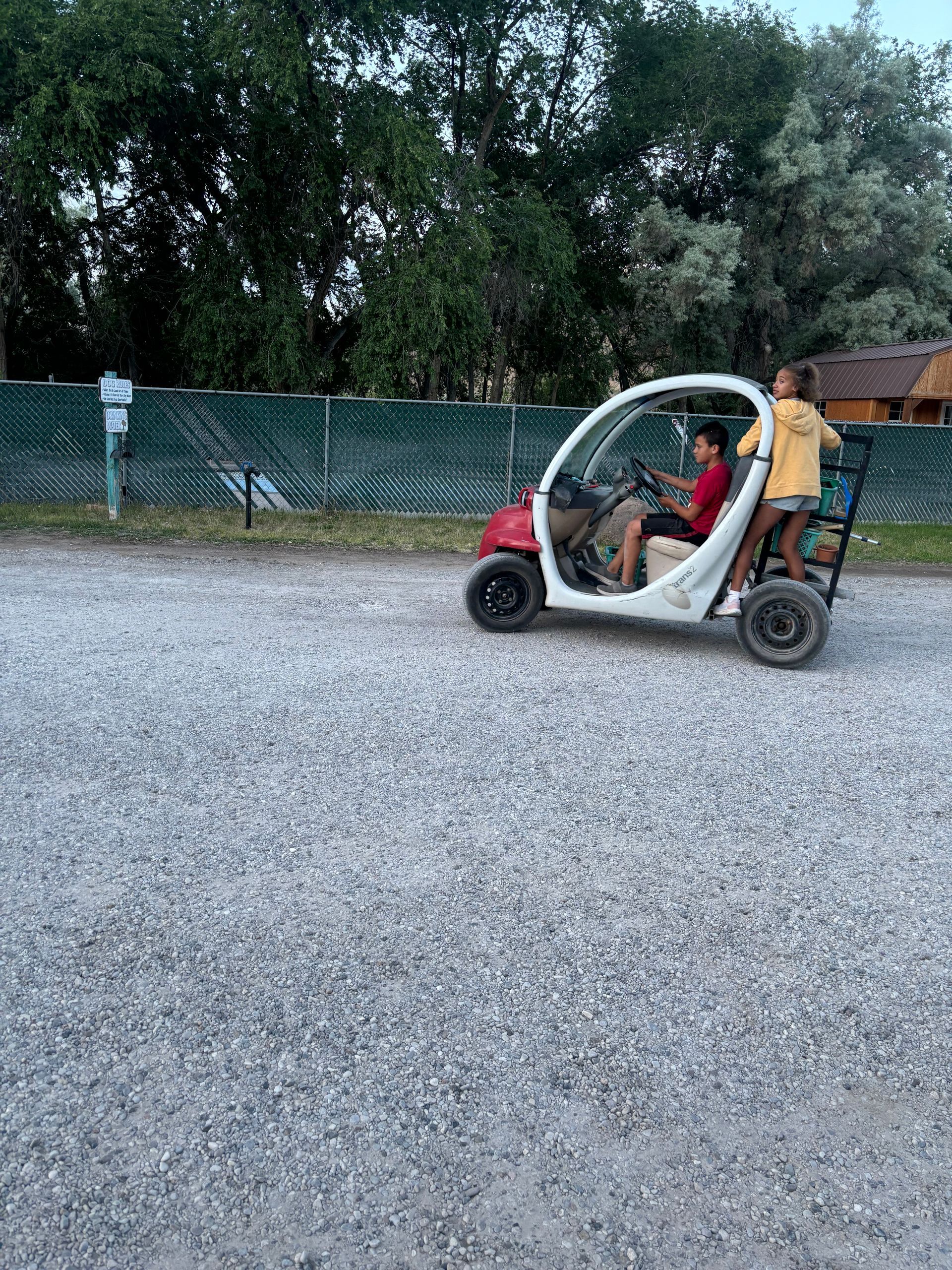 Two children are riding a golf cart on a gravel road.