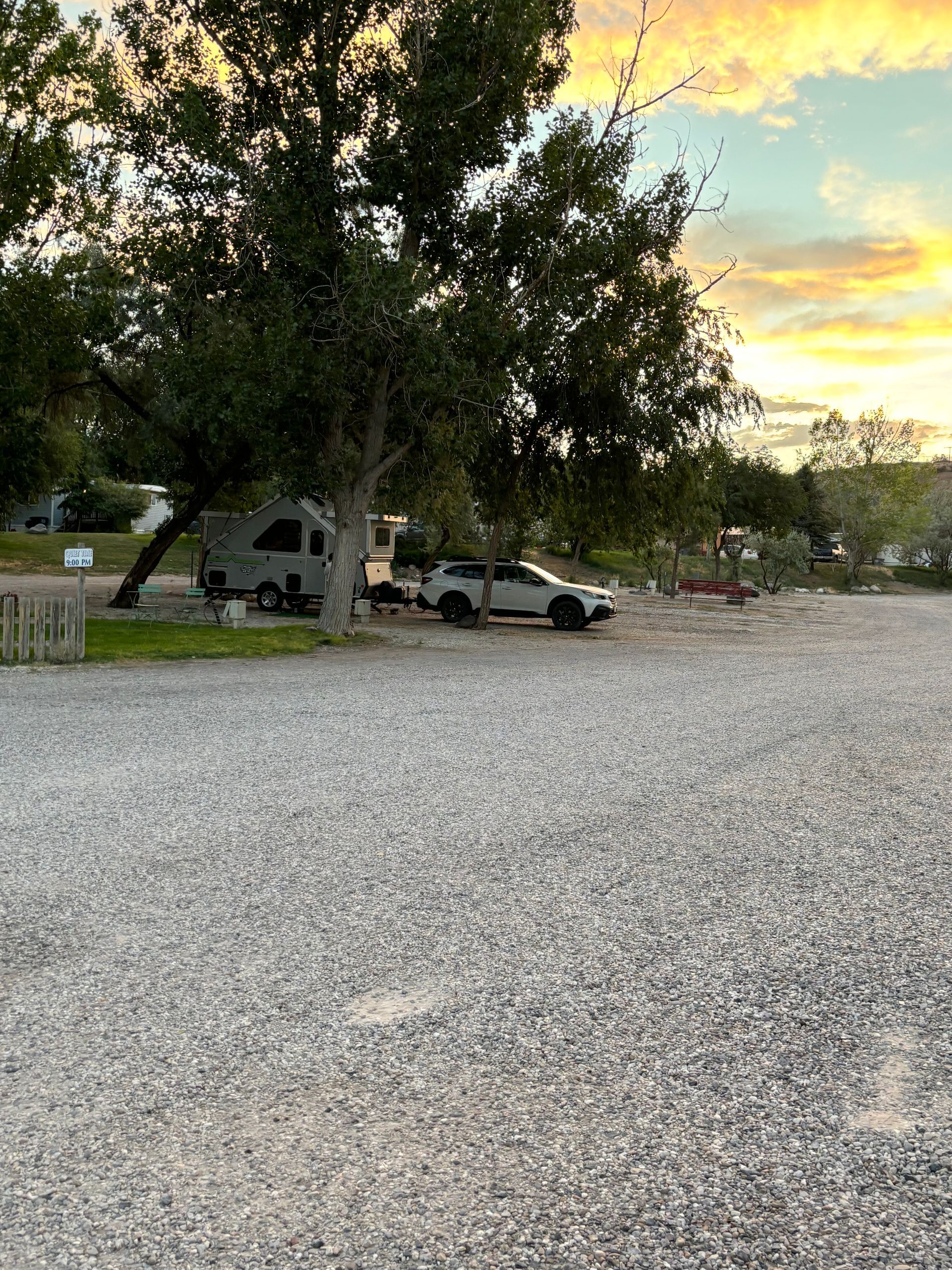 A car is parked in a gravel lot with a sunset in the background.