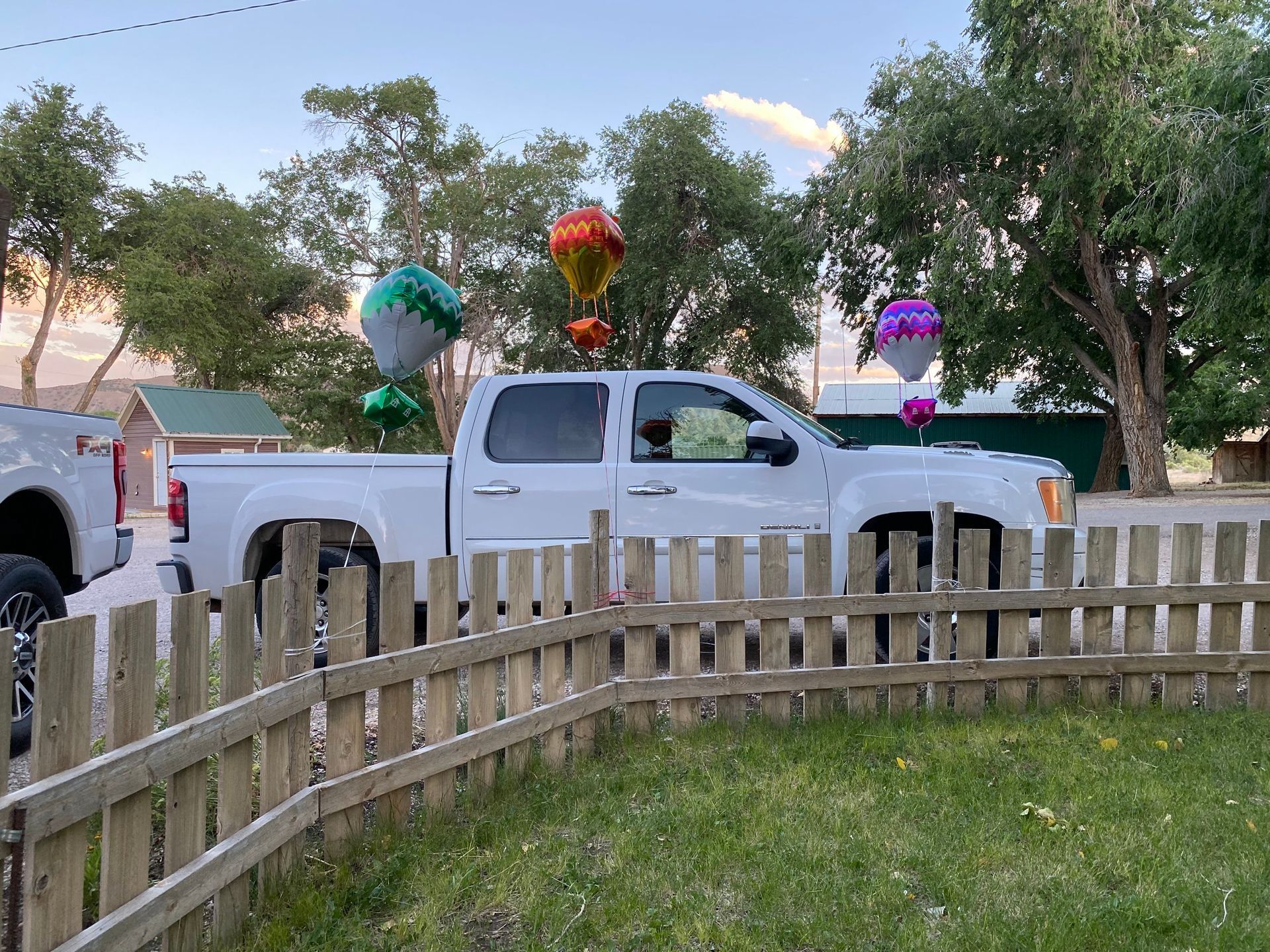 A white truck is parked in front of a wooden fence with balloons in the back.