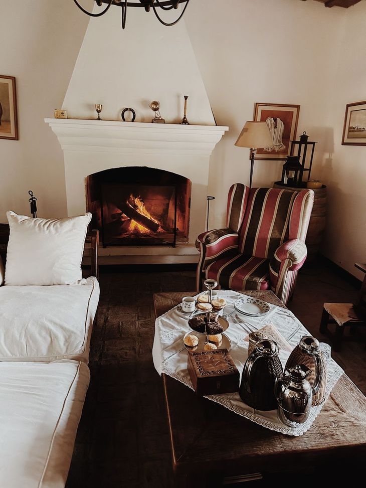 Cozy living room with lit fireplace, white sofa, patterned armchair, and lace-covered coffee table