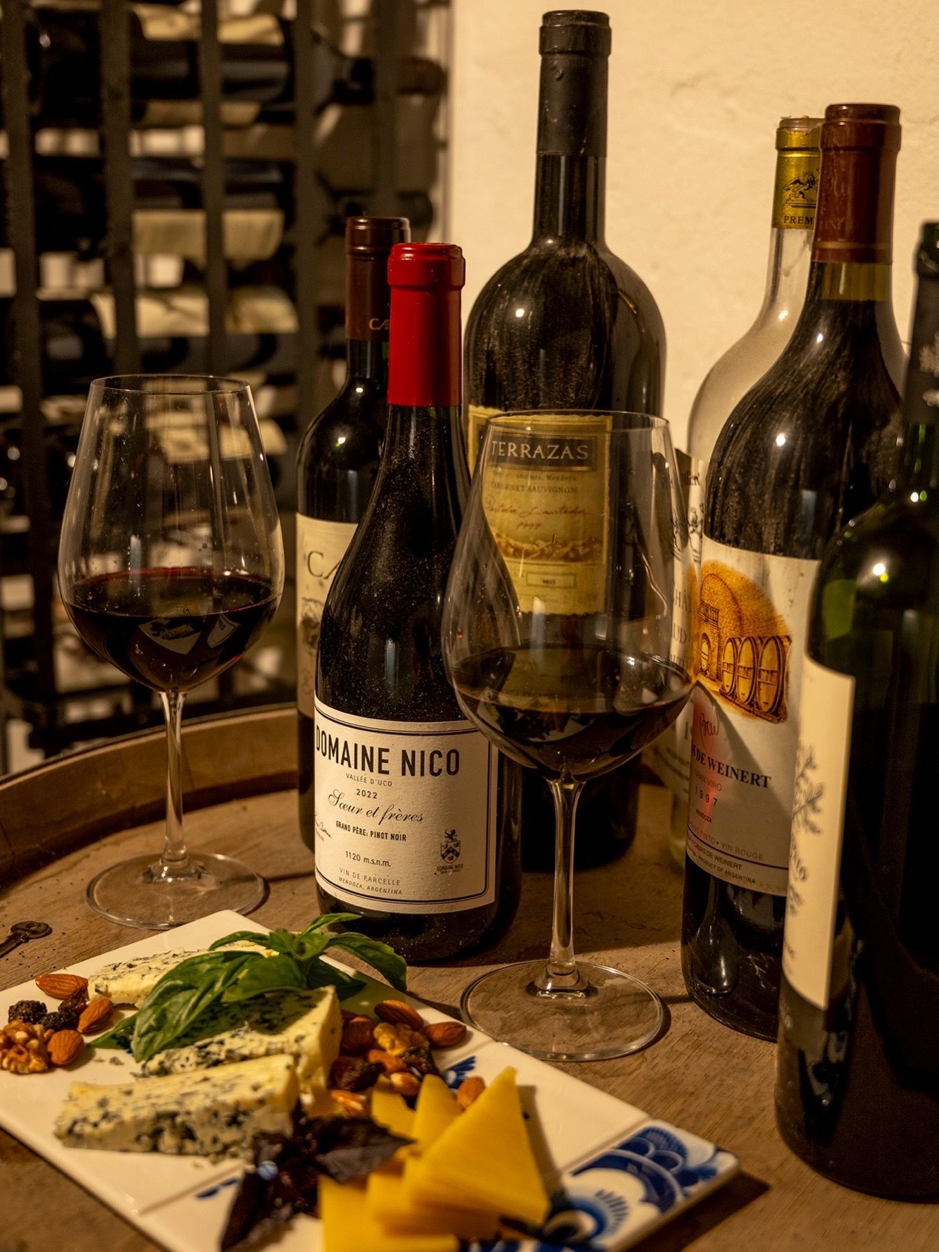 Wine bottles and a glass on a table beside a plate of cheese and garnish