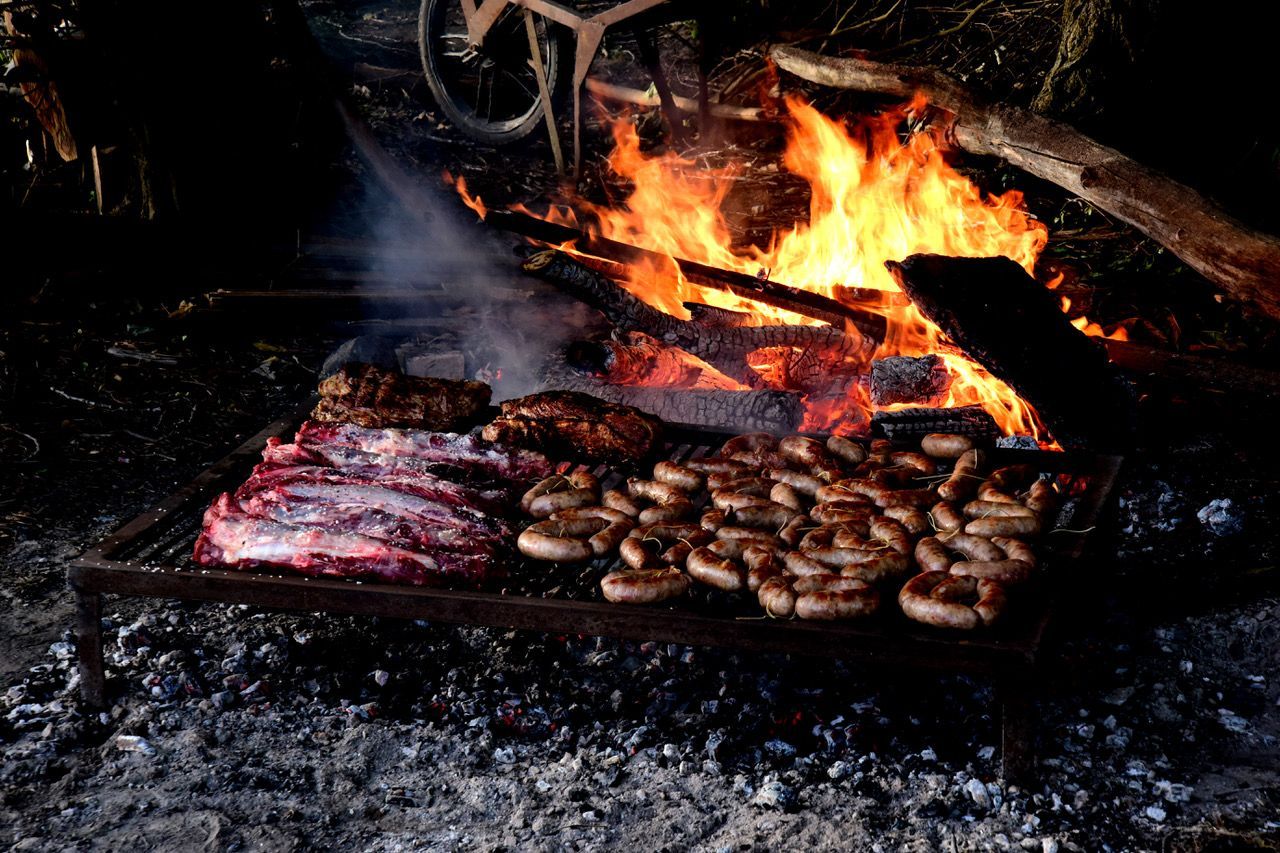 Meat and mushrooms grilling over an open fire with bright flames and smoke