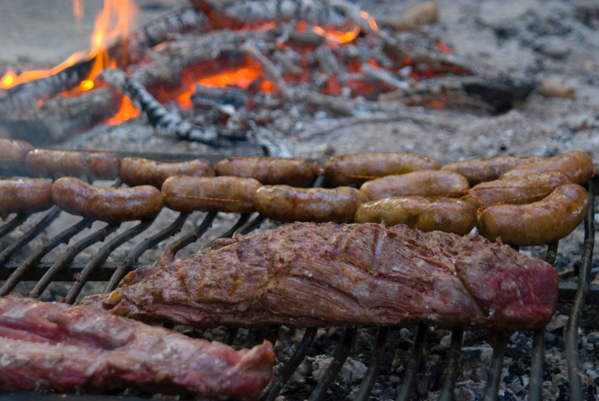Grilled steak sizzling over open flames, browned and charred on a dark grill