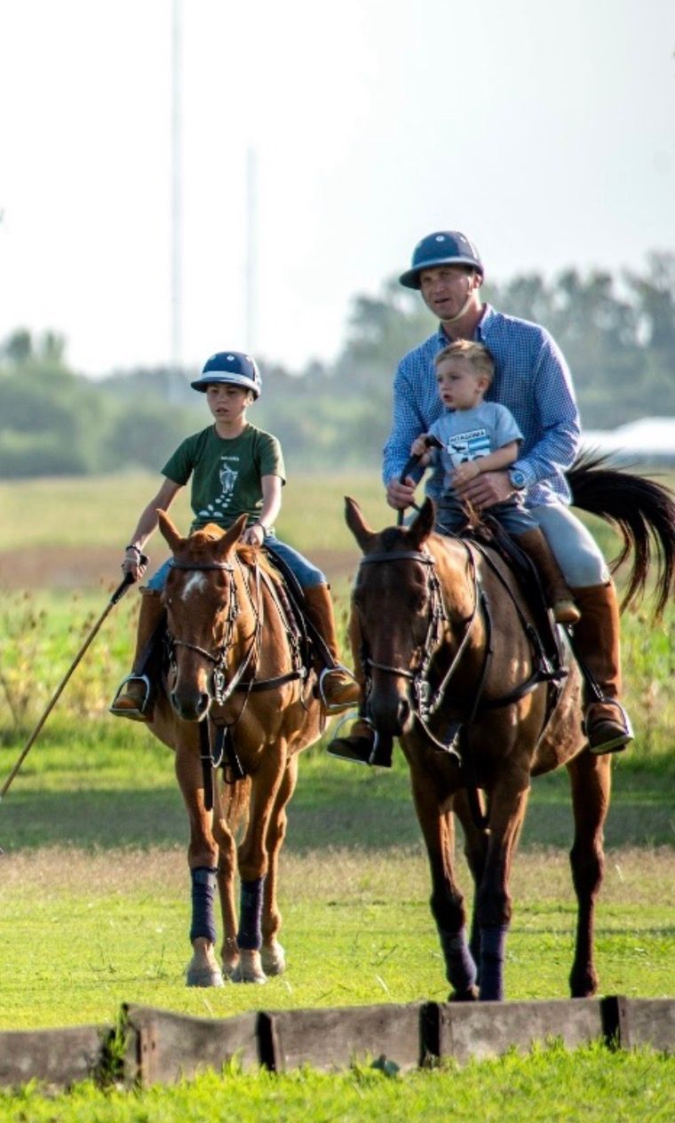 Two riders on horses jump over a field obstacle in a grassy outdoor setting