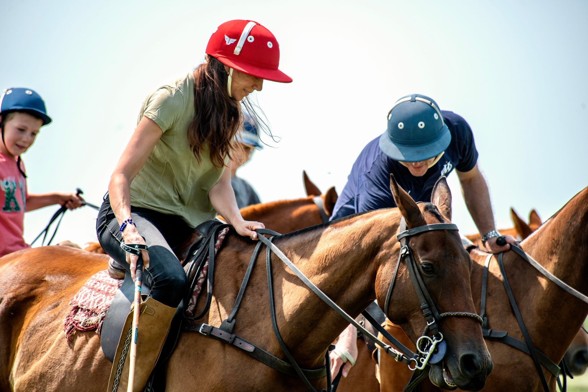 Three jockeys riding horses in a race, two in red and blue helmets in the foreground.