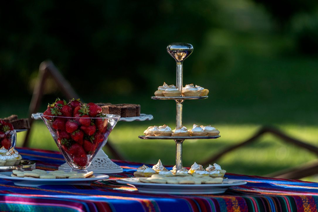 Outdoor dessert table with a glass tray of strawberries and a tiered serving stand on a colorful cloth