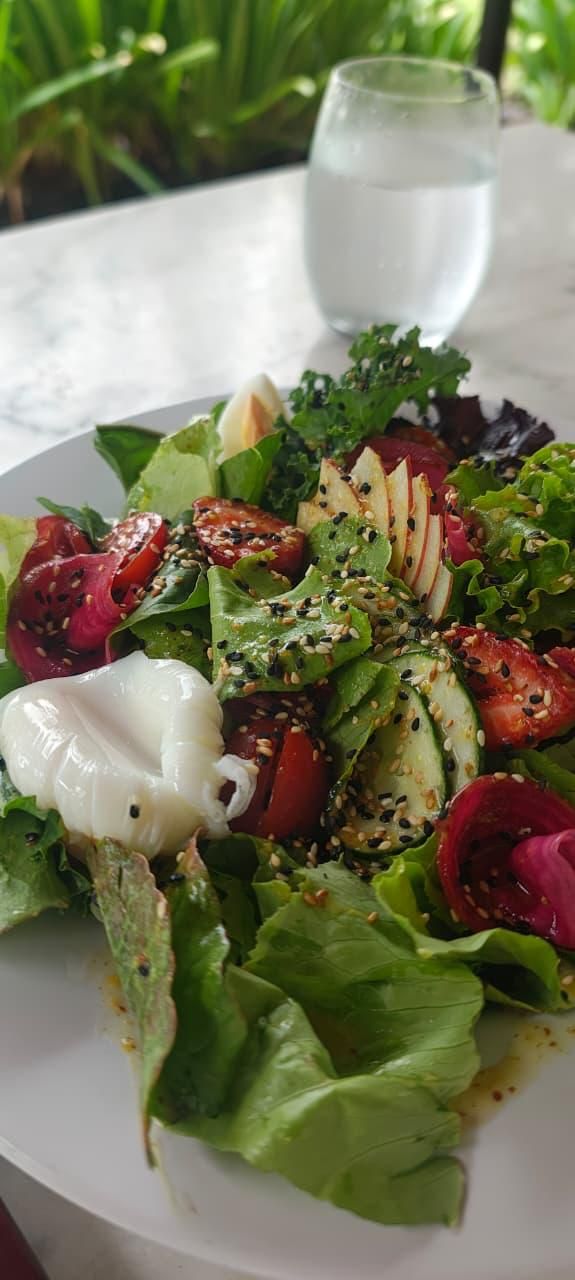 Fresh garden salad with strawberries, avocado, greens, and goat cheese beside a glass of water