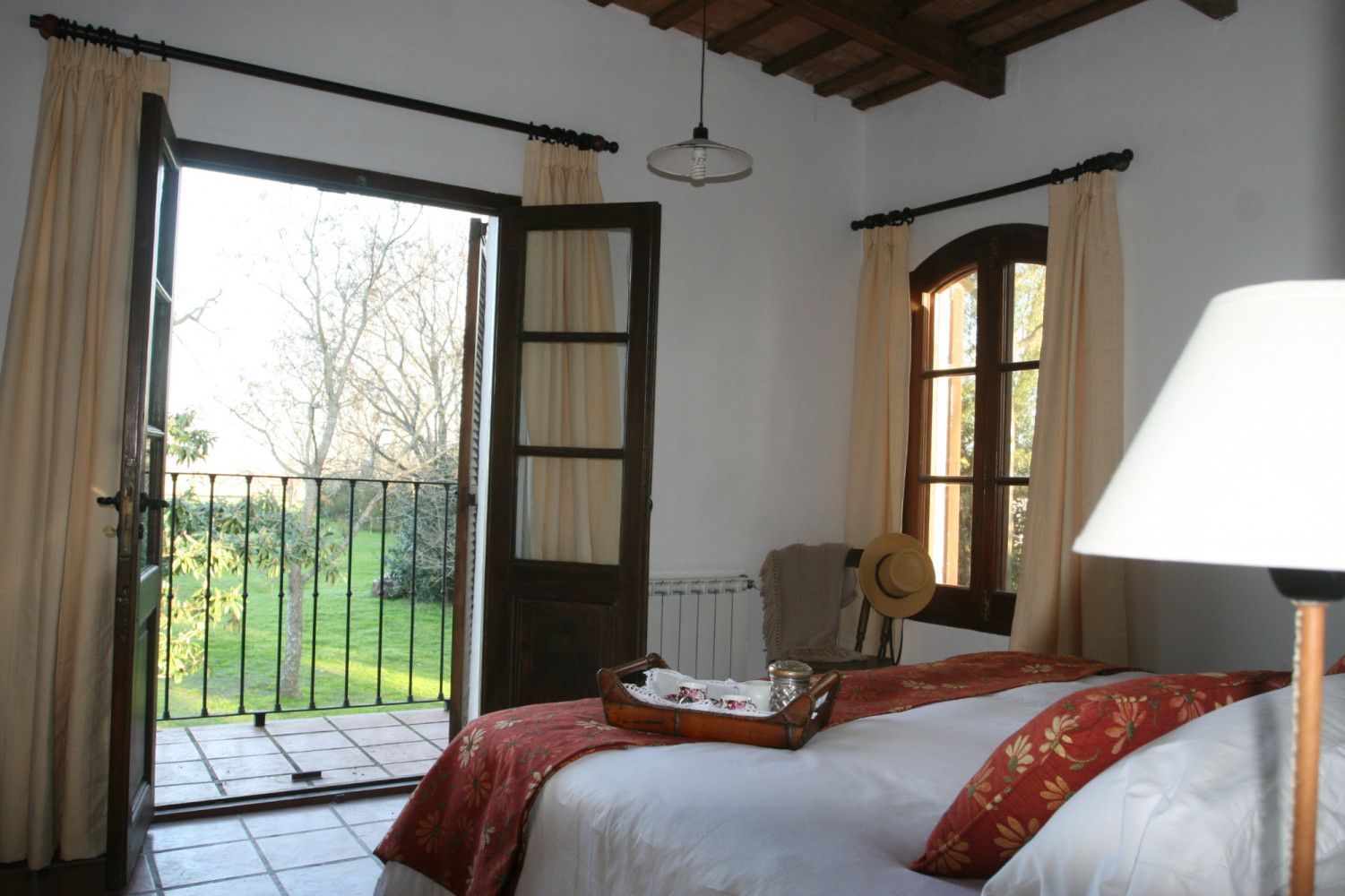 Bright bedroom with bed, rolled towels, desk, open balcony doors, and scenic green field outside.