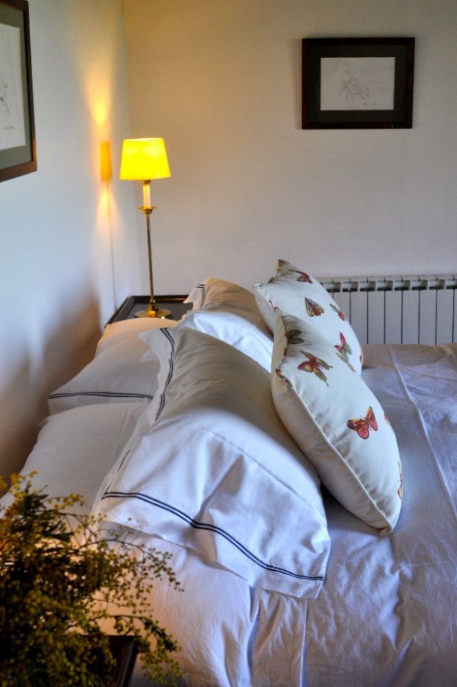 Bed with white bedding and floral pillows in a softly lit bedroom, with a yellow lamp on the nightstand.