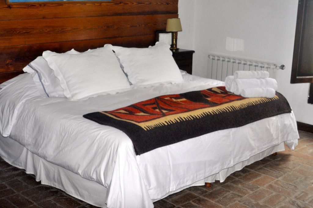 White bed with pillows and red-black throw in a bedroom with wooden headboard and nightstand