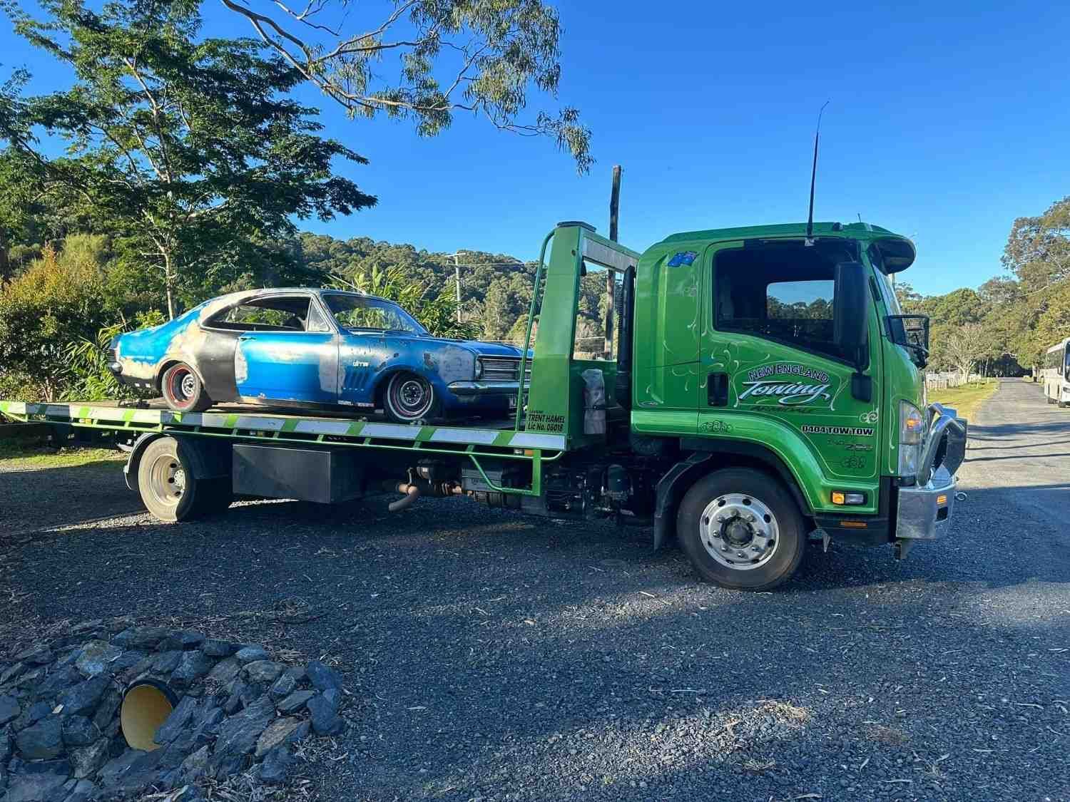 A Green Tow Truck Carrying a Blue Vintage Car with Exposed Metal — New England Towing in Guyra, NSW