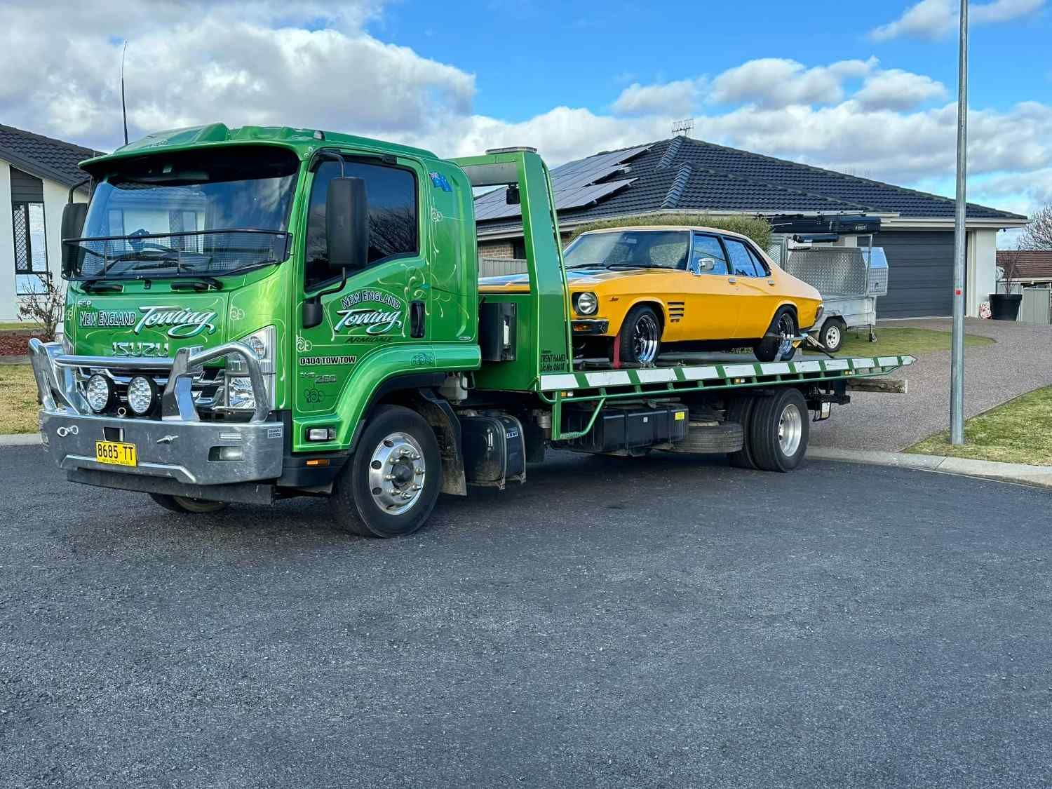 Green Tow Truck Carrying a Yellow Classic Car on A Residential Street — New England Towing in Guyra, NSW