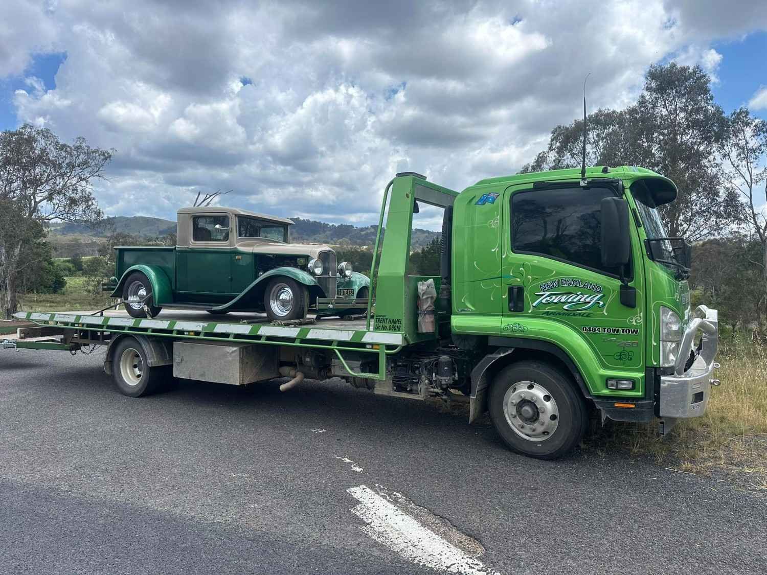 Green Tow Truck Carrying a Vintage Green Car on A Paved Road — New England Towing in Ebor, NSW