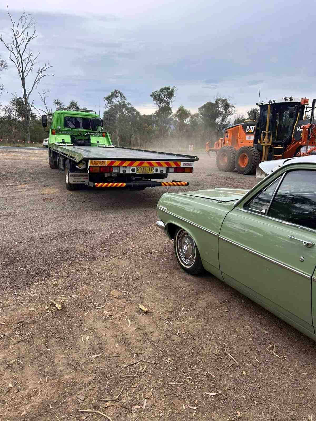 Green Vintage Car Being Towed by A Green Flatbed Tow Truck on A Dirt Lot — New England Towing in Ebor, NSW
