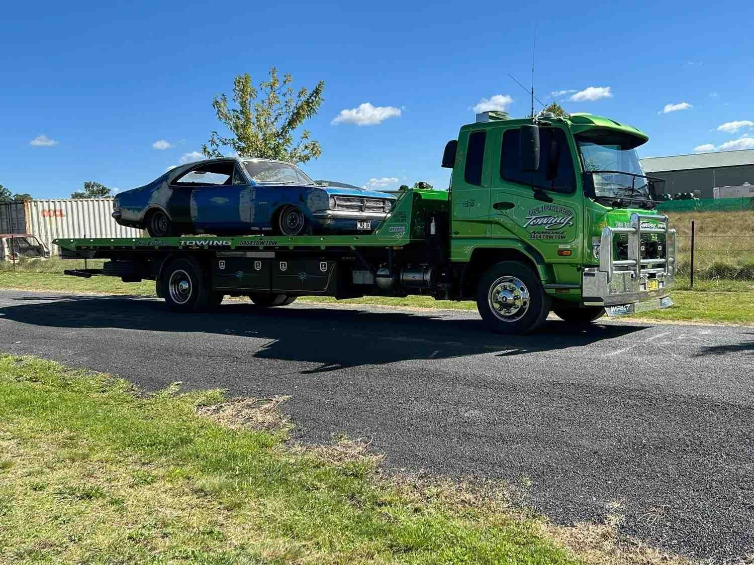 A Green Tow Truck Carrying a Weathered, Blue Car — New England Towing in Walcha, NSW