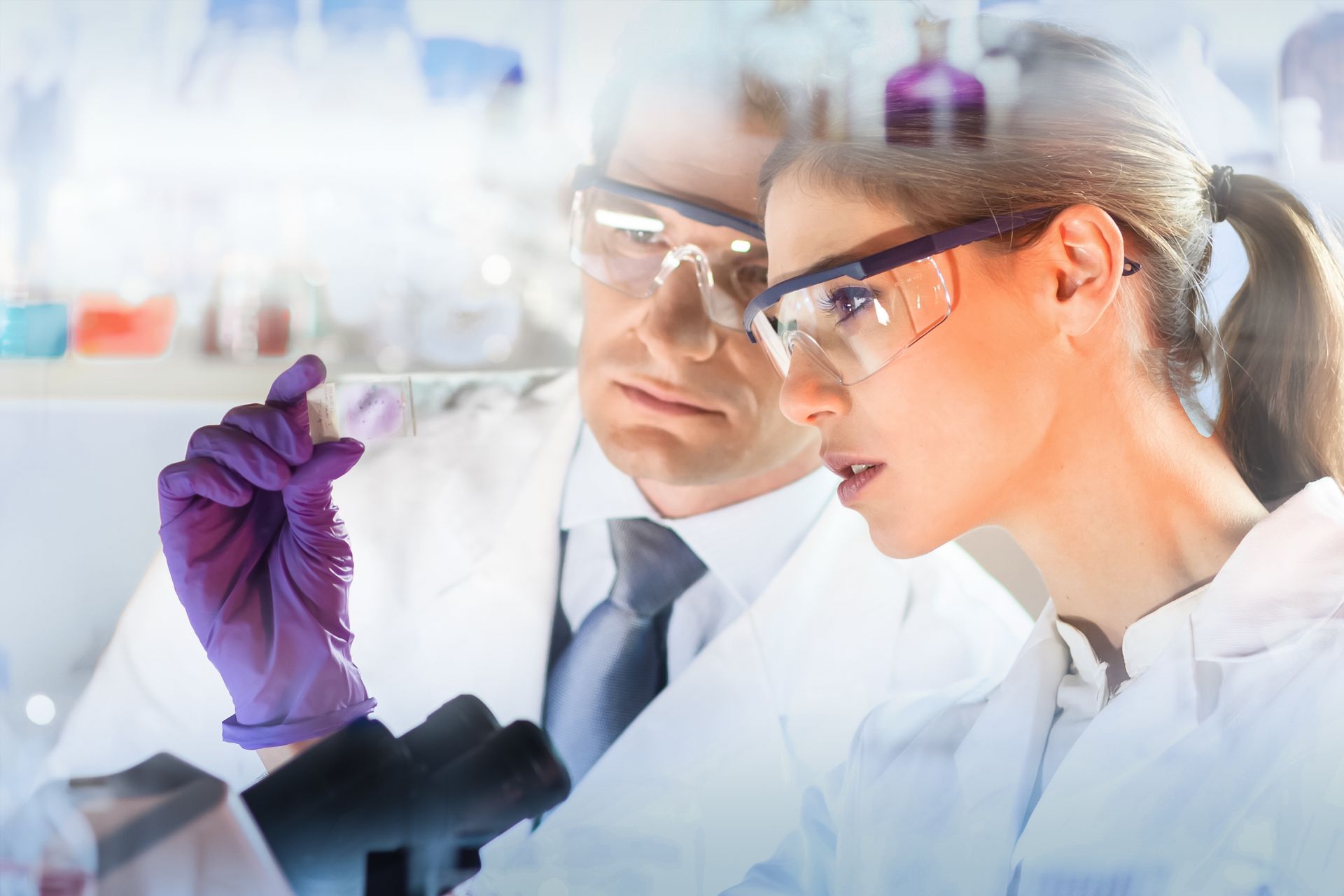 A man and a woman are looking through a microscope in a laboratory.