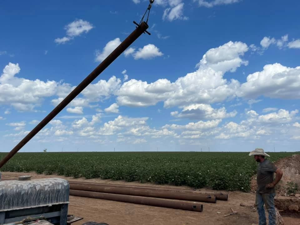Rural irrigation pipe extending over a field, with a worker standing nearby under a blue sky with clouds
