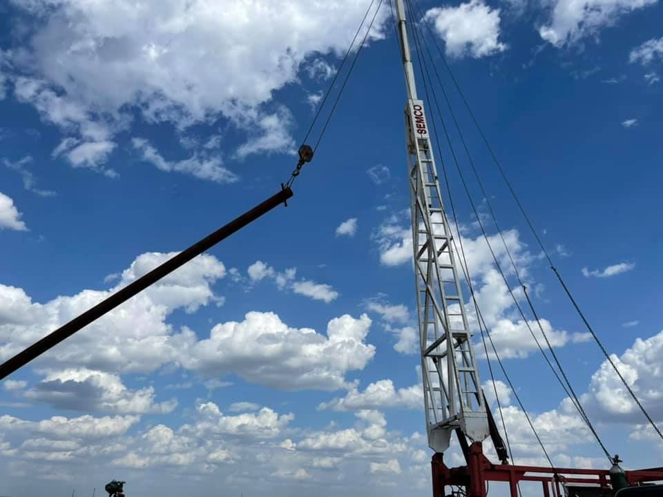 Crane boom lifting a black pipe against a blue sky with scattered clouds