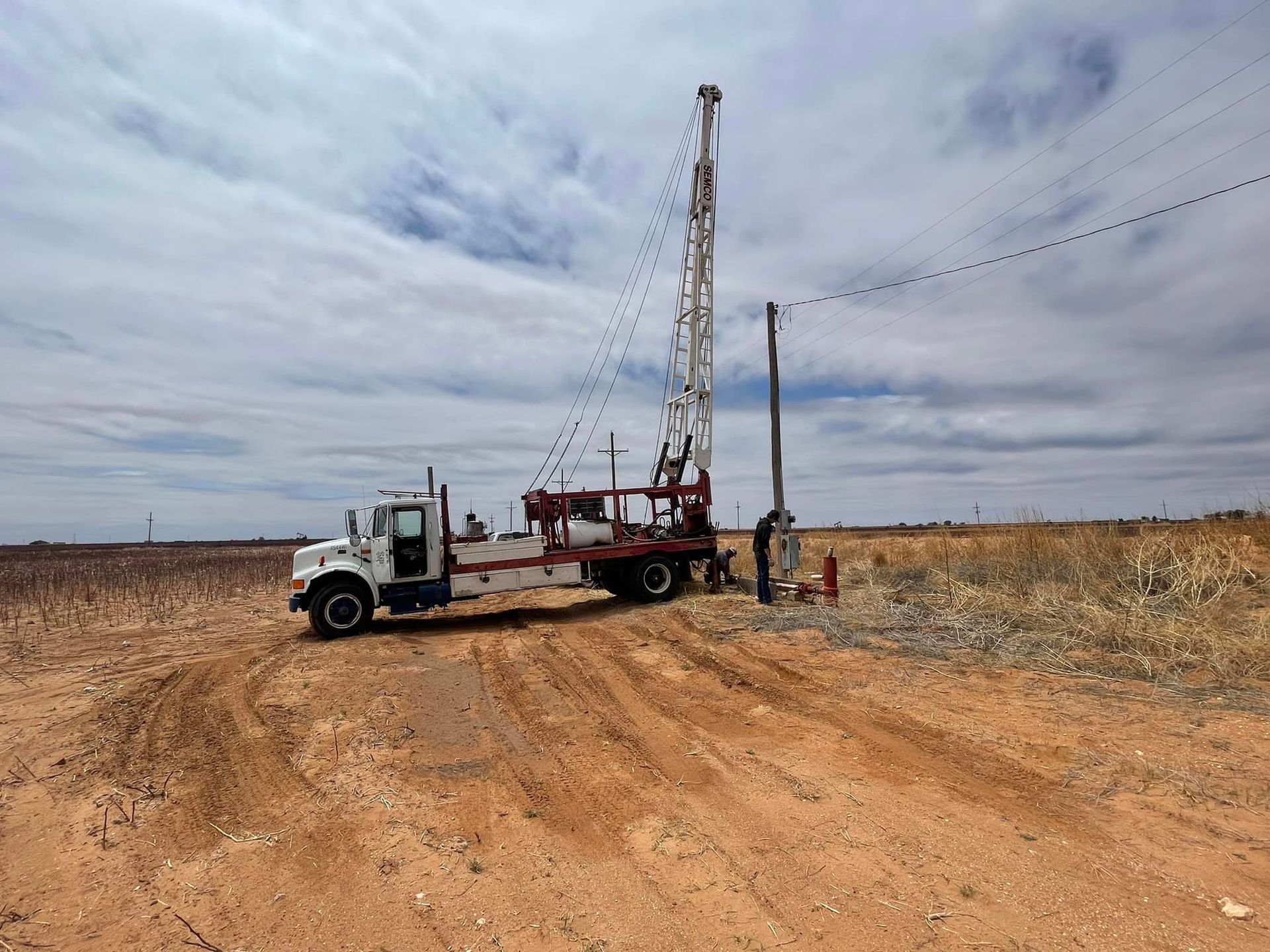 Drilling rig truck on a dirt road in a dry field under a cloudy sky