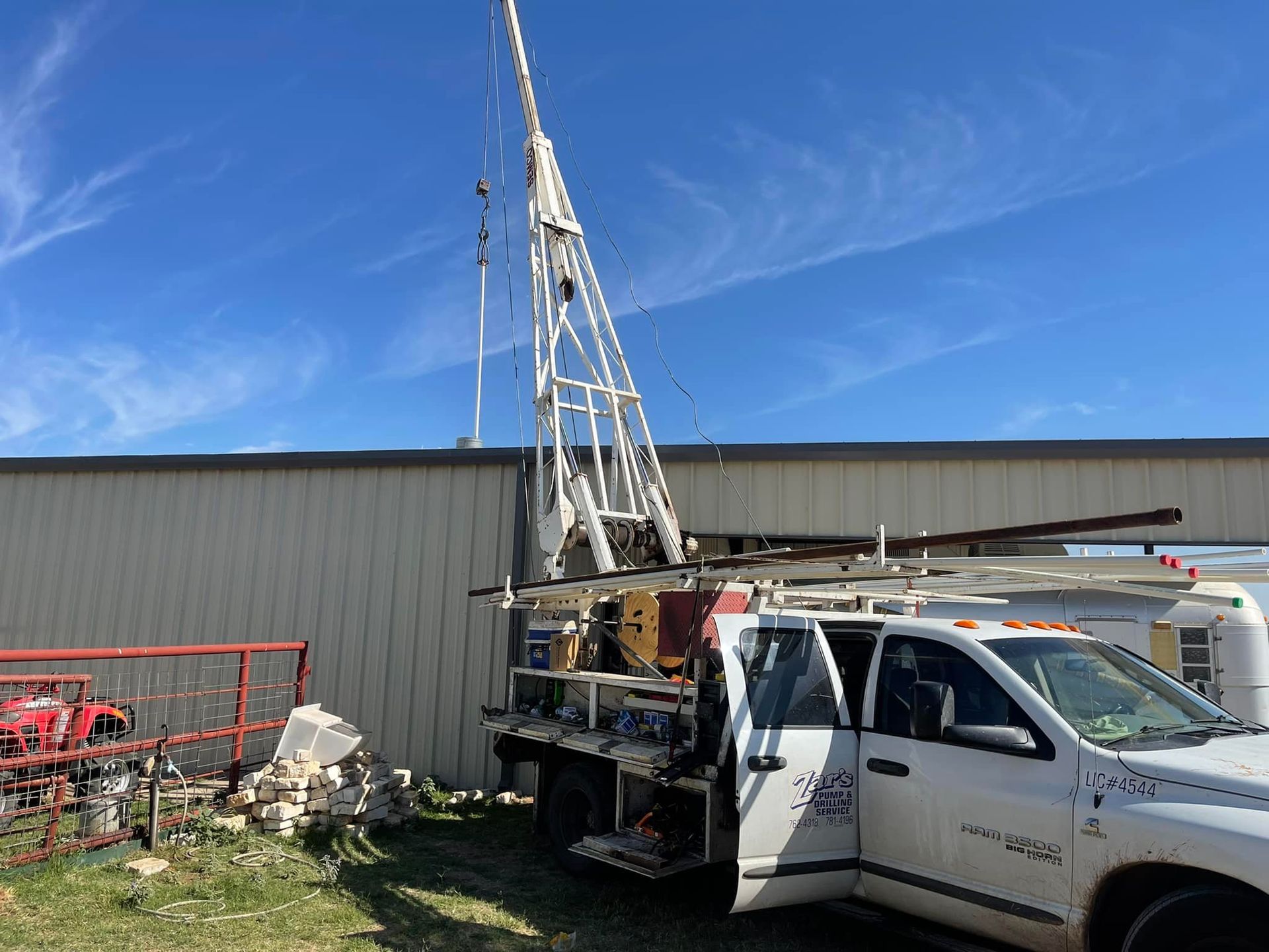 White utility truck with crane parked beside a metal building under a blue sky.