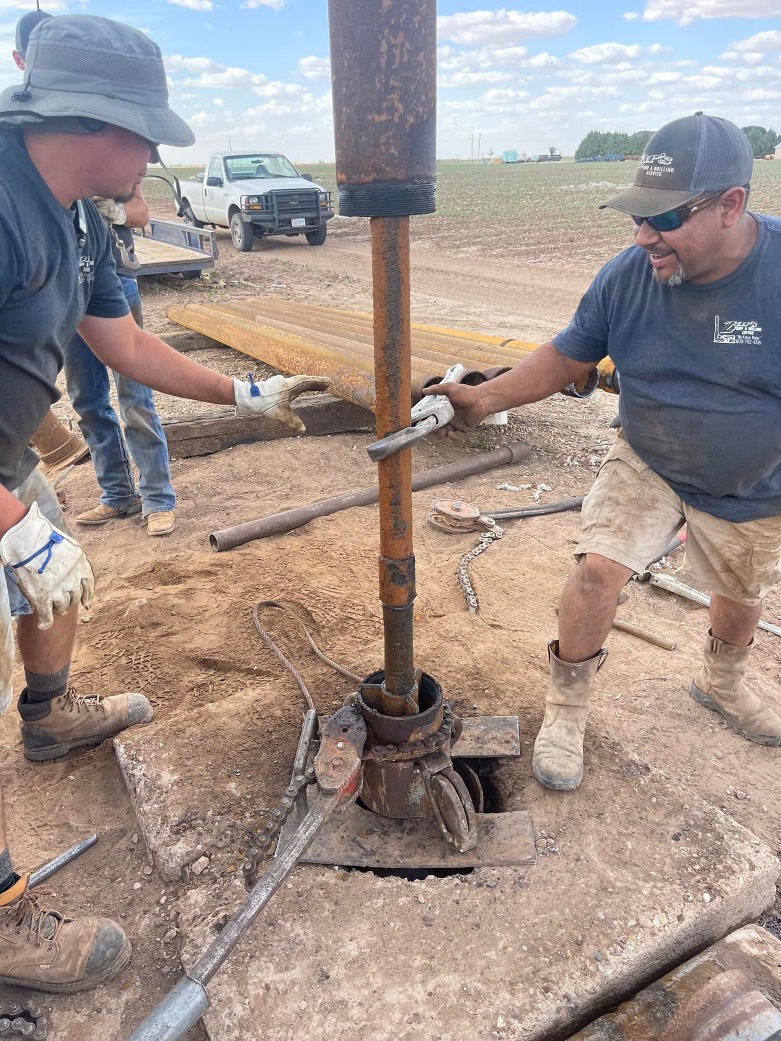 Two workers using a post driver to set a fence post in a muddy field