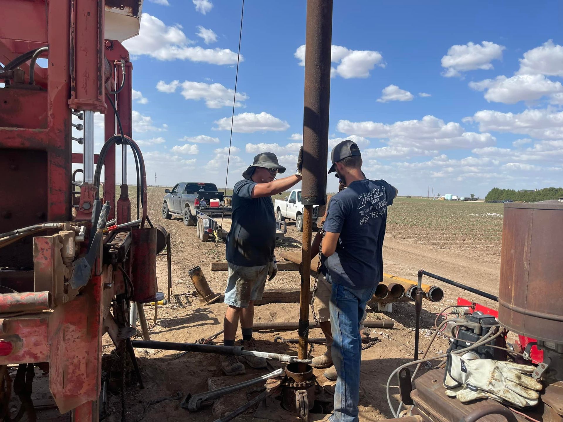 Two workers operating drilling equipment in a dusty oil field under a blue sky