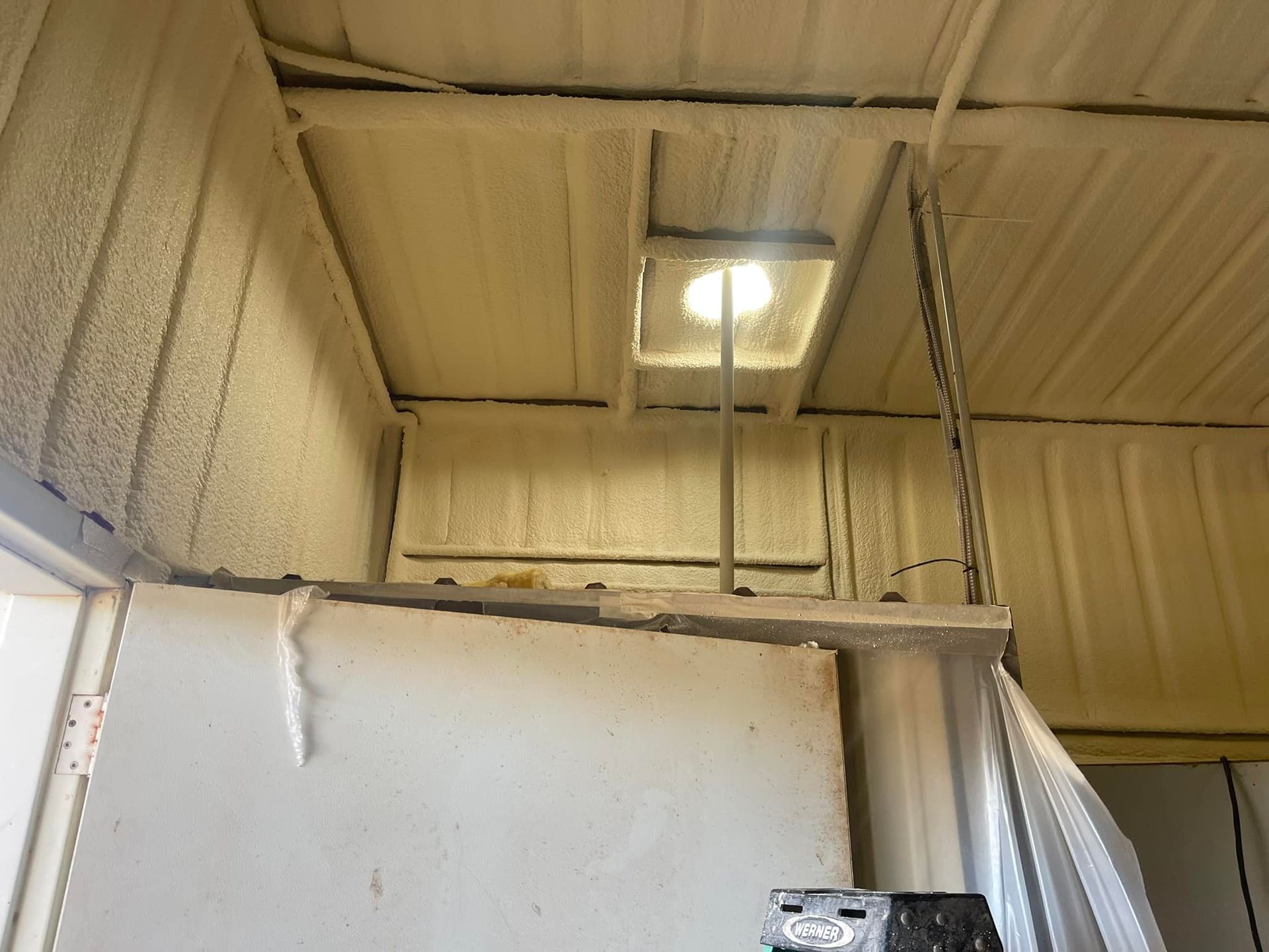 White industrial room with corrugated metal walls, a ceiling light, and a partially open white door panel