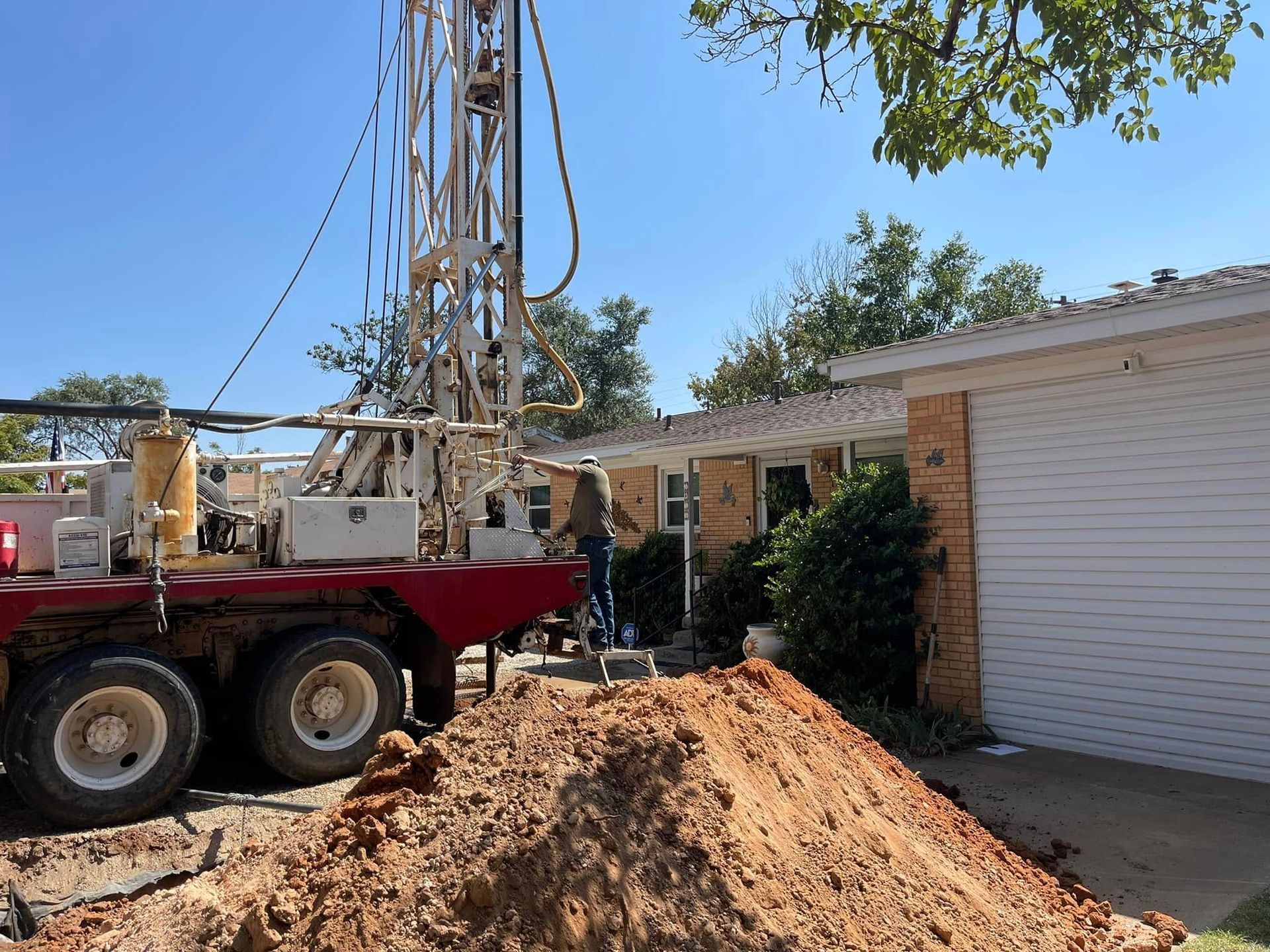 Drilling rig truck beside a house with a large dirt mound in the front yard