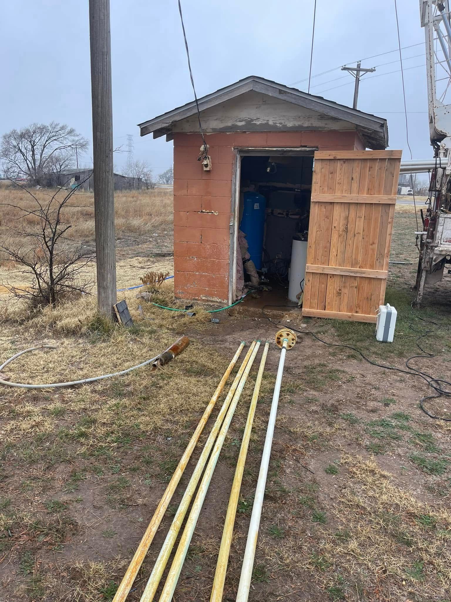 Small brick shed with blue door and wooden siding, with yellow pipes laid on the ground outside.